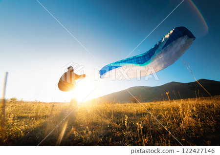 paraglider prepares for a paragliding flight or has already completed it and landed, standing on a hill in the grass, surrounded by a vibrant autumn landscape 122427146