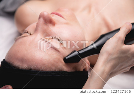 Woman undergoing skin tightening by activating a natural process. A cosmetologist performs a skin rejuvenation procedure in a spa. Aesthetic medical cosmetology Woman undergoing skin tightening by activating a natural process. A cosmetologist performs a skin rejuvenation procedure in a spa. Aesthetic medical cosmetology 122427166