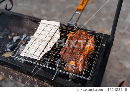 A close-up of seasoned meat and flatbread grilling on a barbecue over hot coals, ready to enjoy 122428346