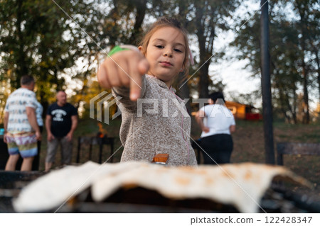 A girl places flatbread on a barbecue grill, participating in outdoor cooking during a family picnic 122428347