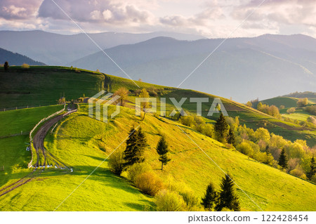 rural area with rolling hills at sunset. travel destination for weekend. cloudy weather. carpathian mountain landscape of ukraine. forest and grassy meadow on the hillside. beautiful scenery 122428454