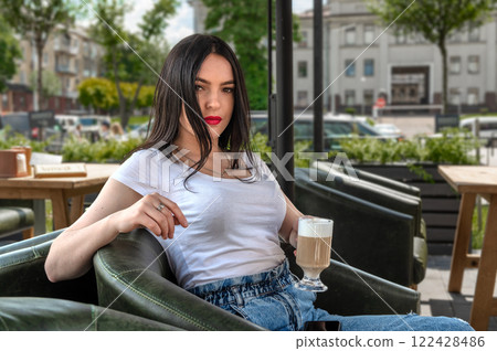 Young woman drinking coffee in cafe outside on sunny day. Woman with cup of cappuccino in hand. 122428486