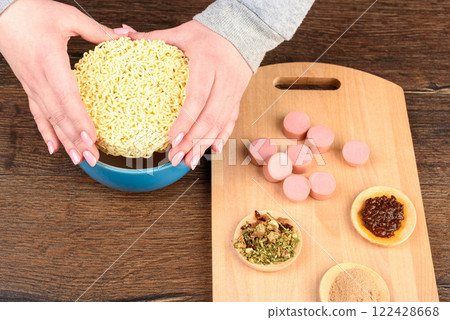 Female hands lowering dry instant noodles into a bowl for cooking. Female hands lowering dry instant noodles into a bowl for cooking. 122428668