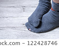 Feet of a person in old socks with a hole, on a wooden floor 122428746