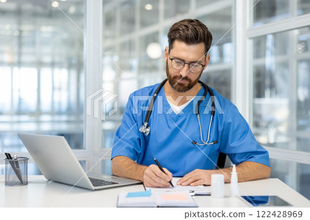 Doctor writing at desk with laptop, conveying professionalism and focus in healthcare environment. Modern office setting enhances theme of medical expertise and dedication. 122428969