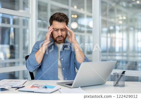 Headache, man holding his head with his hands grimacing in pain, office worker at workplace inside office. Headache, man holding his head with his hands grimacing in pain, office worker at workplace inside office. 122429012