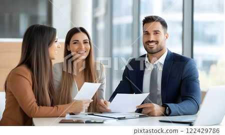 Young couple discussing home options with a real estate agent in a modern office, smiling and holding documents 122429786