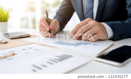 A close-up of hands writing goals in a journal, surrounded by highlighters, charts, and a phone on the desk 122430277