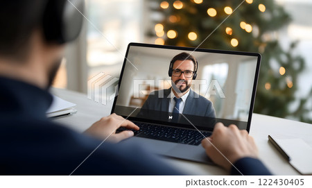 A person in a well-lit home office attending an online meeting on a laptop, wearing headphones and taking notes A person in a well-lit home office attending an online meeting on a laptop, wearing headphones and taking notes 122430405
