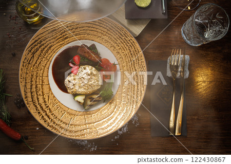 Gold-plated beef steak with grilled vegetables, cherry tomatoes, and a rich sauce. Gourmet dish garnished with edible flowers, served on an elegant plate in a fine dining restaurant 122430867