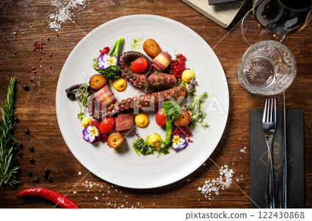 Octopus tentacles with cherry tomatoes, broccoli, and edible flowers. Accompanied by roasted potatoes, yellow sauce, and microgreens. Sophisticated seafood dish in a gourmet restaurant 122430868