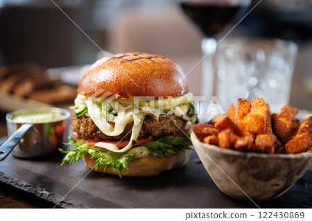 Gourmet vegetarian burger with lettuce, tomato, cheese, and sauce on a brioche bun. Served with a side of sweet potato fries and a metal cup of dipping sauce. Perfect for a healthy meal 122430869