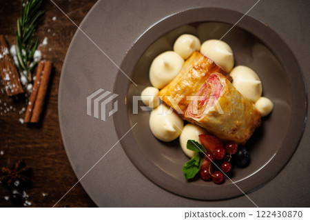 Puff pastry dessert with berry filling. Served with vanilla cream dollops, fresh red currants, blueberries, and mint leaves. Delicious gourmet dessert closeup in modern cuisine restaurant 122430870