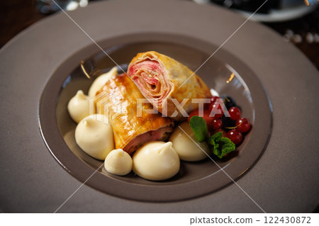 Flaky pastry with berry filling, accompanied by vanilla cream dollops. Garnished with red currants, blueberries, and mint. Elegant dessert closeup in upscale restaurant cuisine Flaky pastry with berry filling, accompanied by vanilla cream dollops. Garnished with red currants, blueberries, and mint. Elegant dessert closeup in upscale restaurant cuisine 122430872