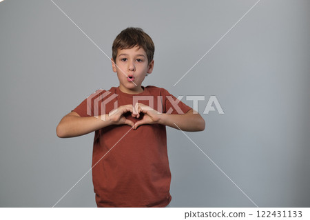 Child shows a heart sign, cheerful and loving. Captures the open-heartedness of youth and the simple ways they express emotions. 122431133