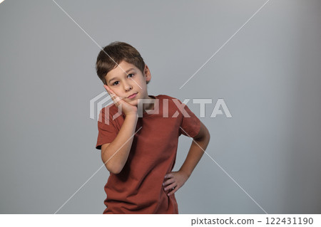 Thoughtful boy rests cheek in hand, looking pensive. Captures the essence of childhood contemplation and the purity of a young mind at rest. Thoughtful boy rests cheek in hand, looking pensive. Captures the essence of childhood contemplation and the purity of a young mind at rest. 122431190