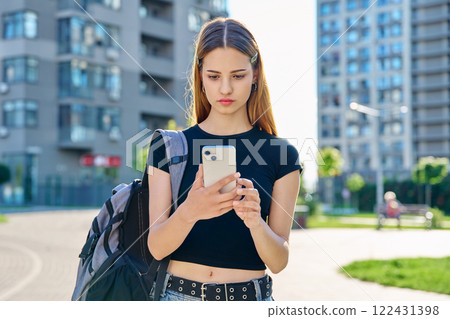 Young serious teenage female using smartphone, modern city background Young serious teenage female using smartphone, modern city background 122431398
