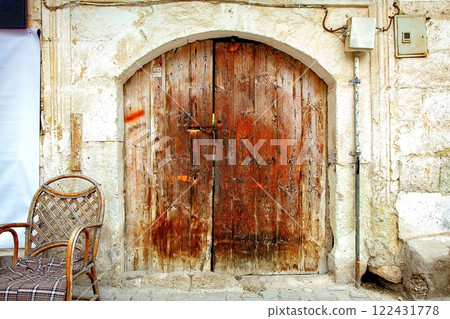 Weathered wooden door adding charm to an ancient stone wall beside a rustic chair 122431778
