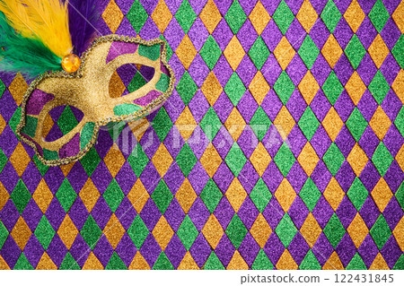 A vibrant Mardi Gras mask lies on a glittery diamond-patterned A vibrant Mardi Gras mask lies on a glittery diamond-patterned 122431845
