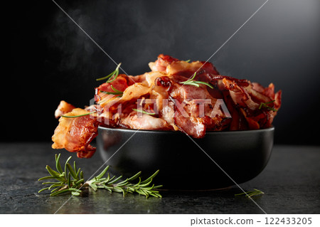 Fried bacon in a black dish with rosemary on a black background. 122433205