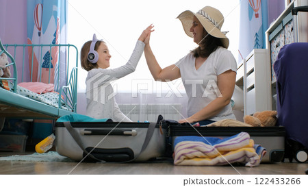 Mother and daughter sit on the floor, cheerfully sorting and folding clothes for their summer vacation in a cozy room 122433266