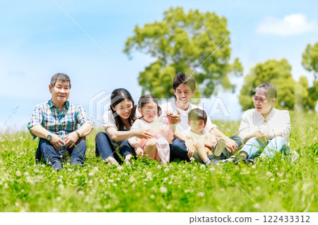 A three-generation family sitting on a meadow in the blue sky 122433312