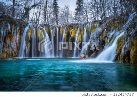 Winter waterfall, lake, frozen trees with icicles in cold evening 122434737