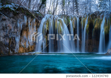 Winter waterfall, lake, frozen trees with icicles in cold evening 122434740
