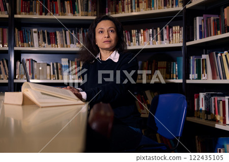 Woman reading in a library surrounded by bookshelves during study time Woman reading in a library surrounded by bookshelves during study time 122435105