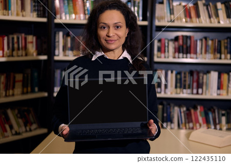 Woman holds laptop in library emphasizing technology and education environments Woman holds laptop in library emphasizing technology and education environments 122435110