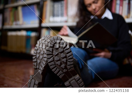 Person reading a book seated in a library with visible boot soles Person reading a book seated in a library with visible boot soles 122435138
