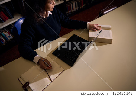 Woman studying at a desk with a laptop and library books 122435145