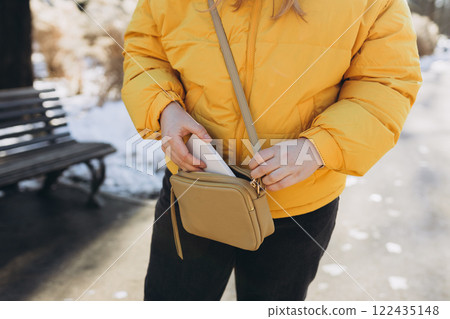 Closeup of woman's hands taking out smartphone from purse outdoors. Young stylish woman taking cellphone out of handbag. Crop anonymous female putting modern cellphone into fashionable handbag 122435148
