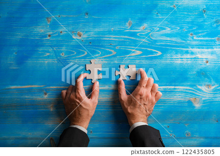Top view of hands of a businessman holding two blank matching puzzle pieces 122435805
