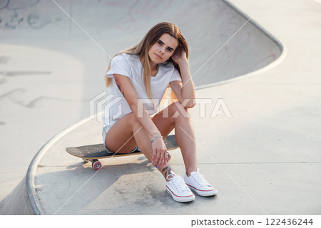 Young attractive girl in a white sweatshirt and knee socks in a skatepark with skateboard. 80s-90s spirit, Miami style. Mock up. 122436244