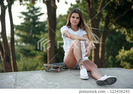 Young attractive girl in a white sweatshirt and knee socks in a skatepark with skateboard. 80s-90s spirit, Miami style. Mock up. 122436245