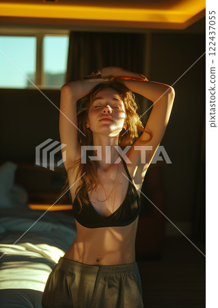 A woman is standing in a bedroom with her arms raised A woman is standing in a bedroom with her arms raised 122437055