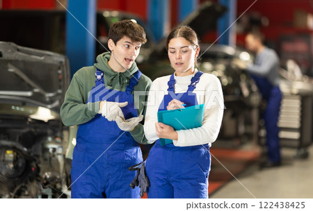 Car service manager discusses car repair problems with mechanic. He takes notes on paper 122438425