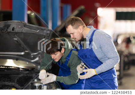 Two auto mechanics work together to diagnose an engine under the hood of a car in repair shop 122438453