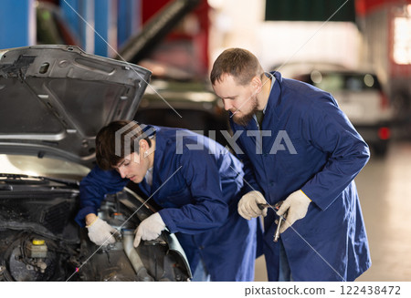 Two auto mechanics work together to diagnose an engine under the hood of a car in repair shop Two auto mechanics work together to diagnose an engine under the hood of a car in repair shop 122438472