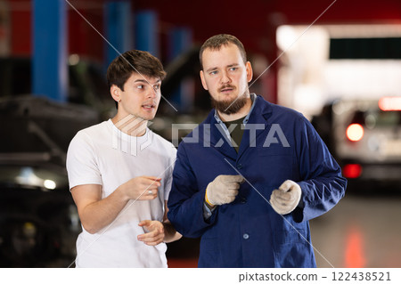 guy talks to a car service mechanic about car repairs guy talks to a car service mechanic about car repairs 122438521