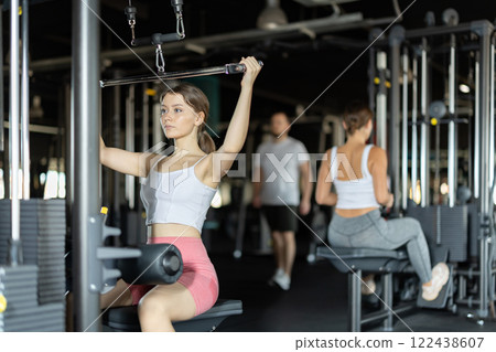 Slender athletic woman work out muscles of hands on cable crossover machine in fitness club 122438607