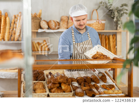 Baker places hot croissants on display in shop 122438619