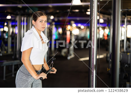 Young woman exercising her arms on cable machine Young woman exercising her arms on cable machine 122438629