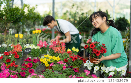Cheerful young asian girl choosing blooming potted petunias 122438679