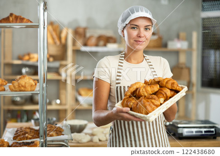 Enthusiastic young female baker offering fresh croissants in bakery 122438680