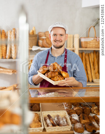 Selling fresh croissants in bakery - Baker places hot croissants on display 122438681