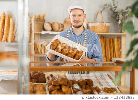 Man seller stands at bakery counter with basket filled with fresh croissants. Man seller stands at bakery counter with basket filled with fresh croissants. 122438682