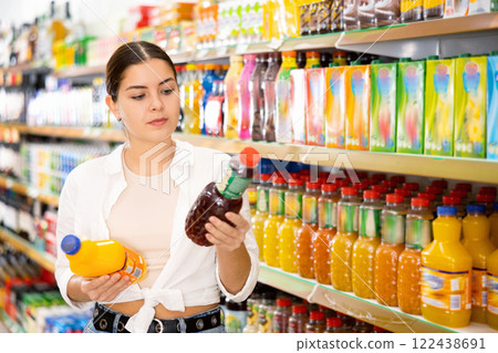 Young girl reading labels on bottles with juices in store 122438691