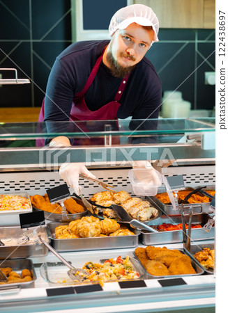 Salesman serving ready-to-eat dishes from deli counter in supermarket Salesman serving ready-to-eat dishes from deli counter in supermarket 122438697
